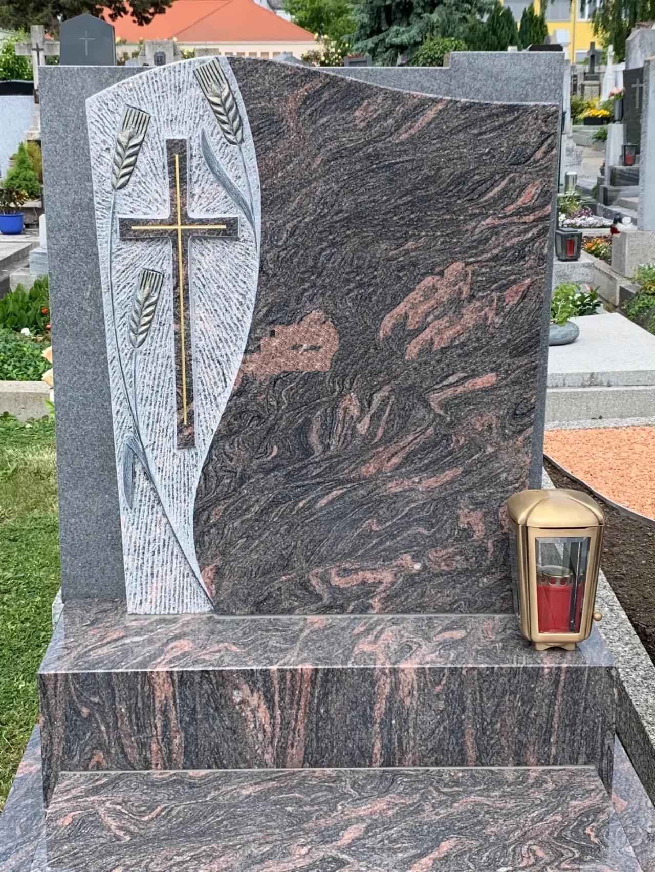Eine würdevolle Grabanlage in Niederösterreich: Dieser Grabstein aus Himalaya Naturstein ist ein individuelles Grabdenkmal mit einem Ornament aus Kreuz und Getreide sowie passendem Grabzubehör.