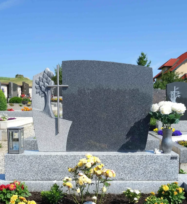  Ein Doppelgrab mit einem zweiteiligen Grabstein aus Naturstein. Die Tarn-Einfassung, das individuelle Ornament und das Aluminium-Kreuz sowie das passende Grabzubehör wurden von unserem Steinmetz in Krems gefertigt.