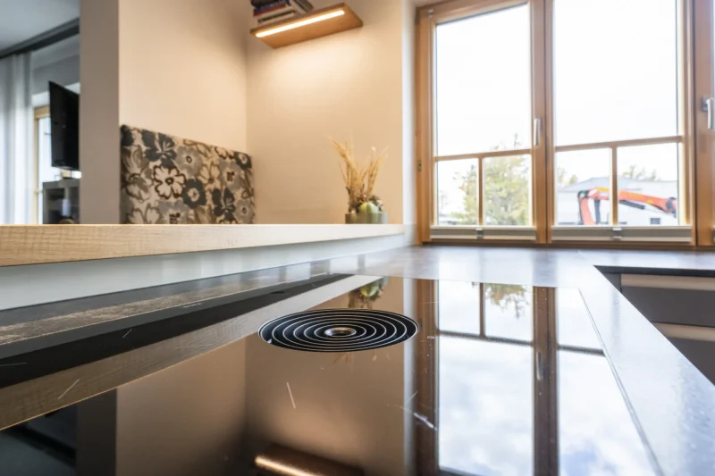 Nahaufnahme einer grauen Naturstein-Küchenarbeitsplatte mit präzise verbautem, flächenbündigem Ceranfeld. Hochwertige Steinmetz-Arbeit aus der Region Krems, Niederösterreich.