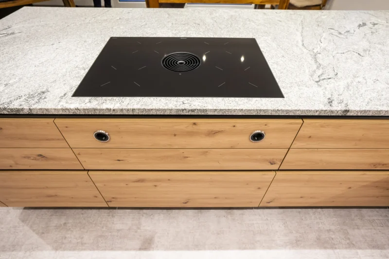 Kochinsel aus poliertem Granit mit flächenbündigem Ceranfeld. Eine präzise Steinmetz-Arbeit aus Naturstein, die Design und Funktionalität vereint. Gefertigt in Niederösterreich.